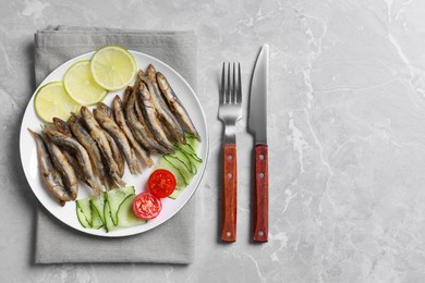 Delicious fried anchovies with lime, cucumber and tomato served on grey marble table, flat lay. Space for text