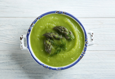 Photo of Delicious asparagus soup in bowl on white wooden table, top view