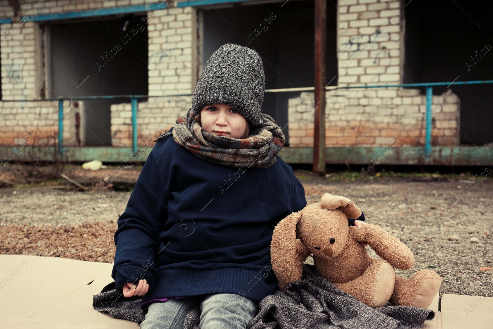 Photo of Poor little girl with toy rabbit on dirty street