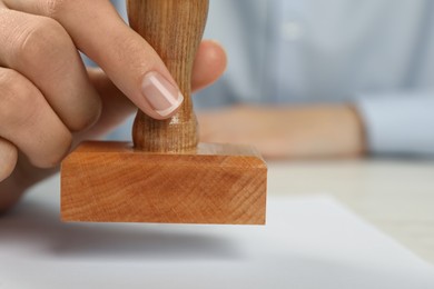 Photo of Woman stamping blank sheet of paper at white wooden table, closeup