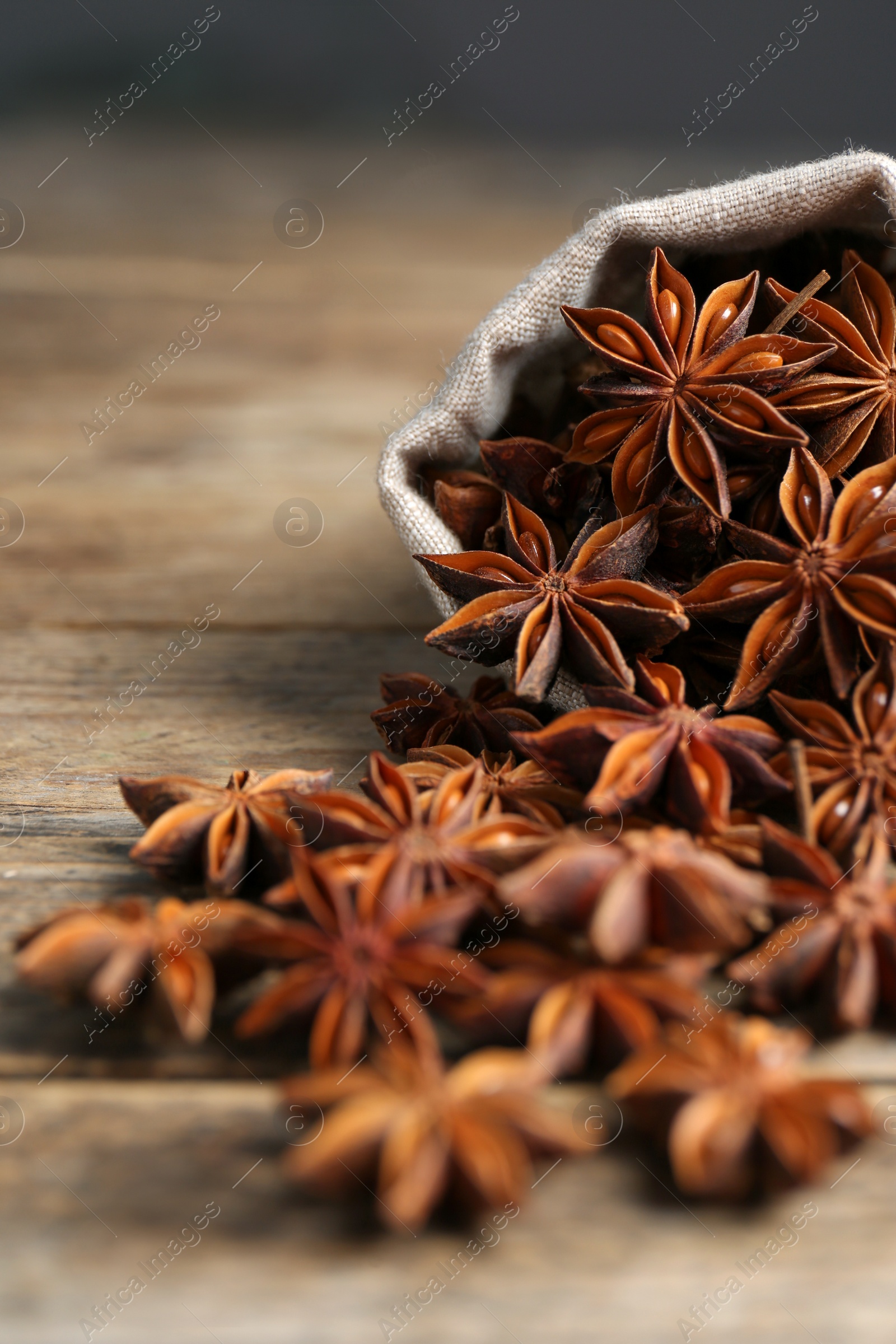 Photo of Overturned bag with aromatic anise stars on wooden table, closeup