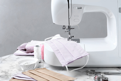 Photo of Sewing machine, homemade protective masks and craft accessories on white marble table