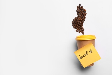 Photo of Note with word Decaf attached to takeaway cup and coffee beans on white background, flat lay. Space for text