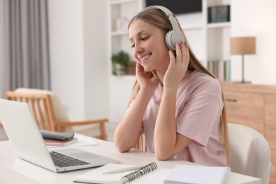 Photo of Online learning. Teenage girl in headphones looking on laptop at table