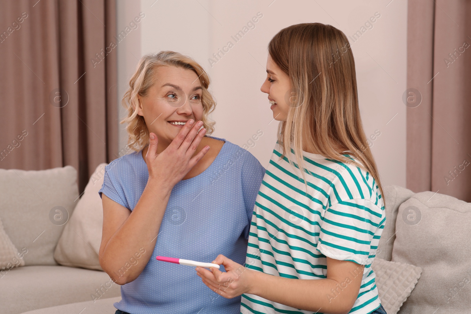 Photo of Young woman showing her mother pregnancy test at home. Grandparent reaction to future grandson