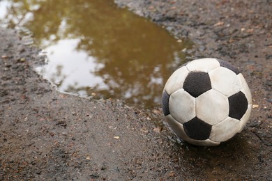 Dirty soccer ball near puddle on ground, space for text