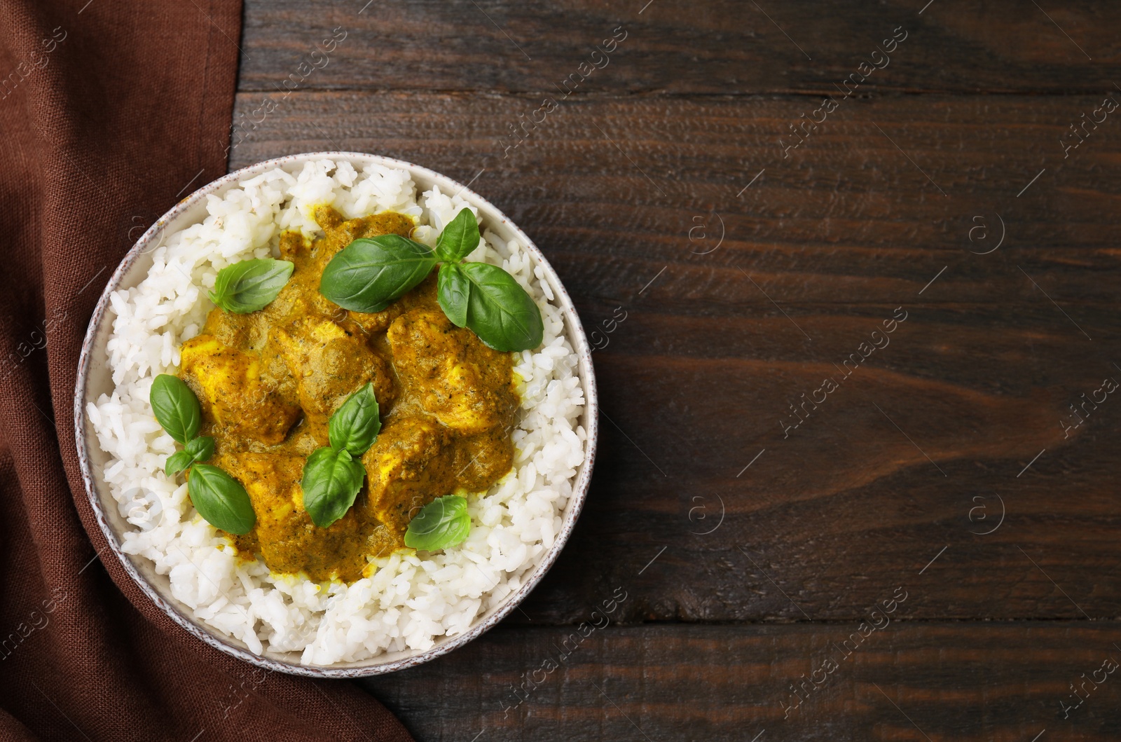 Photo of Delicious rice and chicken with curry sauce served on wooden table, top view. Space for text