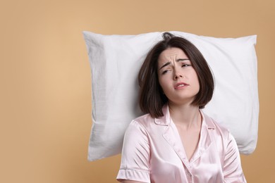 Photo of Unhappy young woman with pillow on beige background, space for text. Insomnia problem