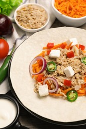 Photo of Delicious tortilla with tuna, vegetables and cheese on wooden table, closeup. Cooking shawarma