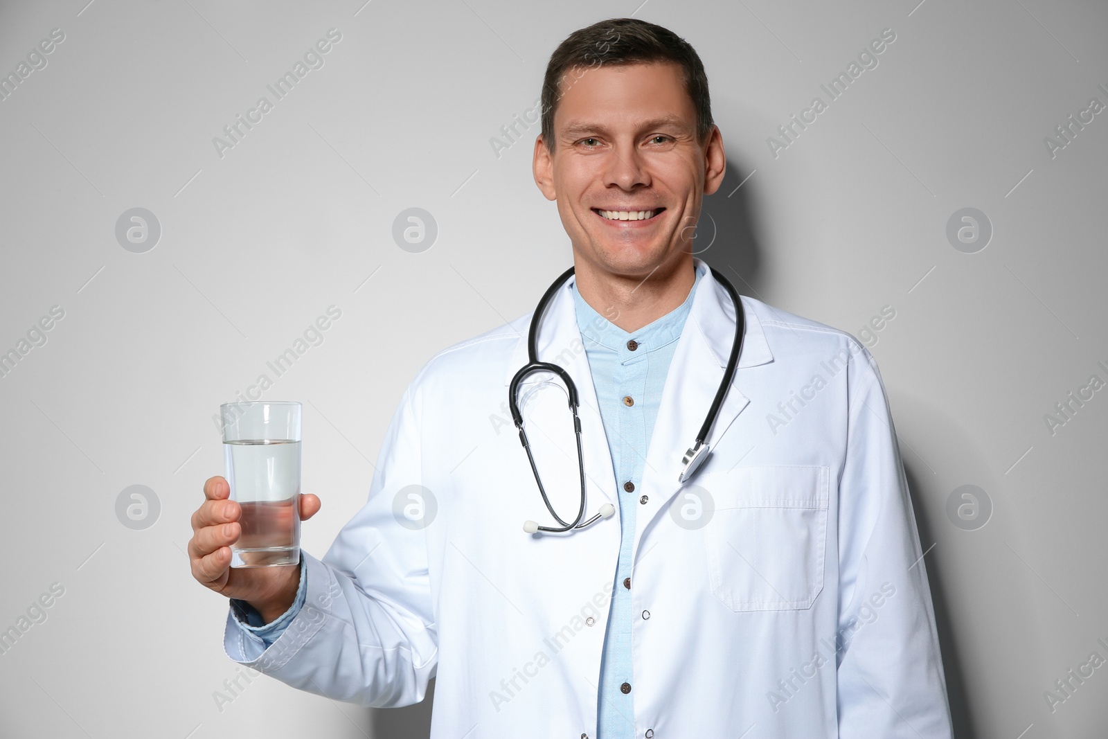 Photo of Nutritionist holding glass of pure water on light grey background