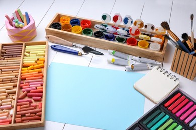 Photo of Blank sheet of paper, colorful chalk pastels and other drawing tools on white wooden table. Modern artist's workplace