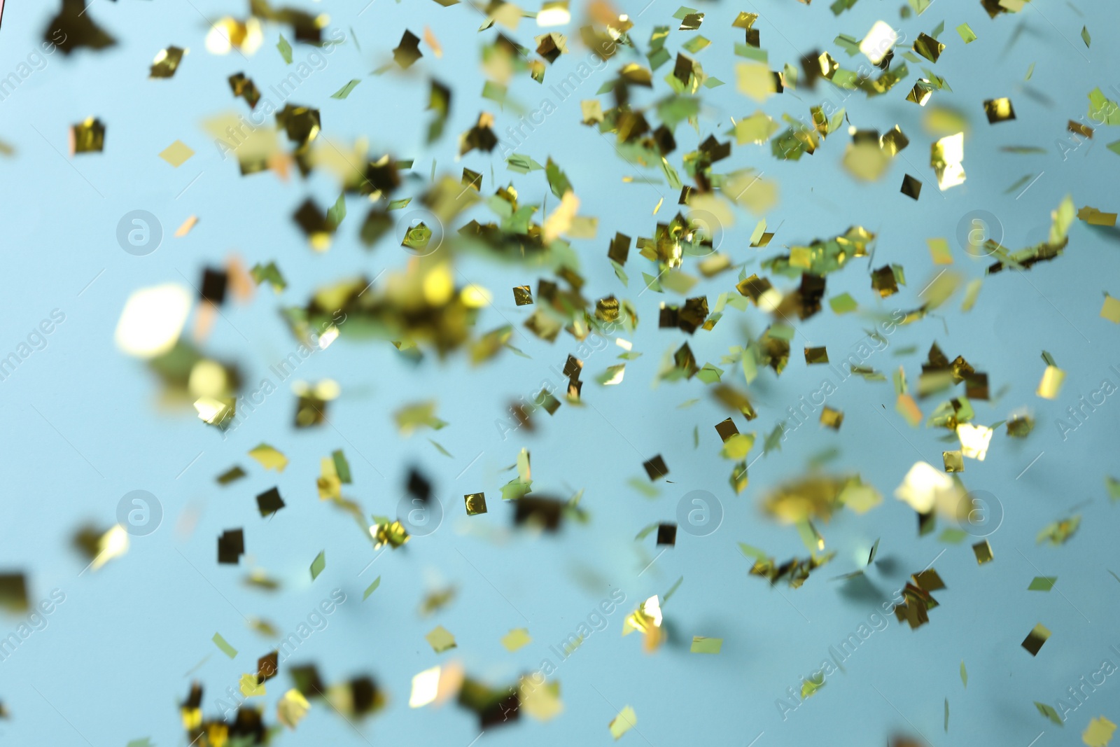 Photo of Shiny golden confetti falling down on light blue background