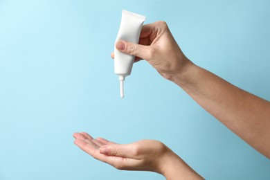 Photo of Woman applying cosmetic cream from tube onto her hand on light blue background, closeup