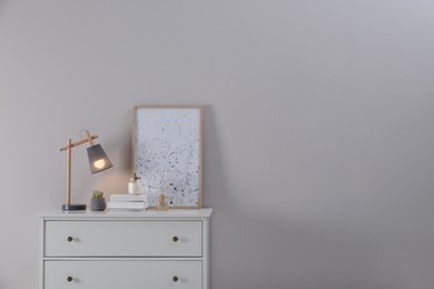 Photo of White chest of drawers, lamp and decor in room, space for text. Interior design