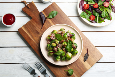 Photo of Delicious Brussels sprouts with bacon on white wooden table, flat lay