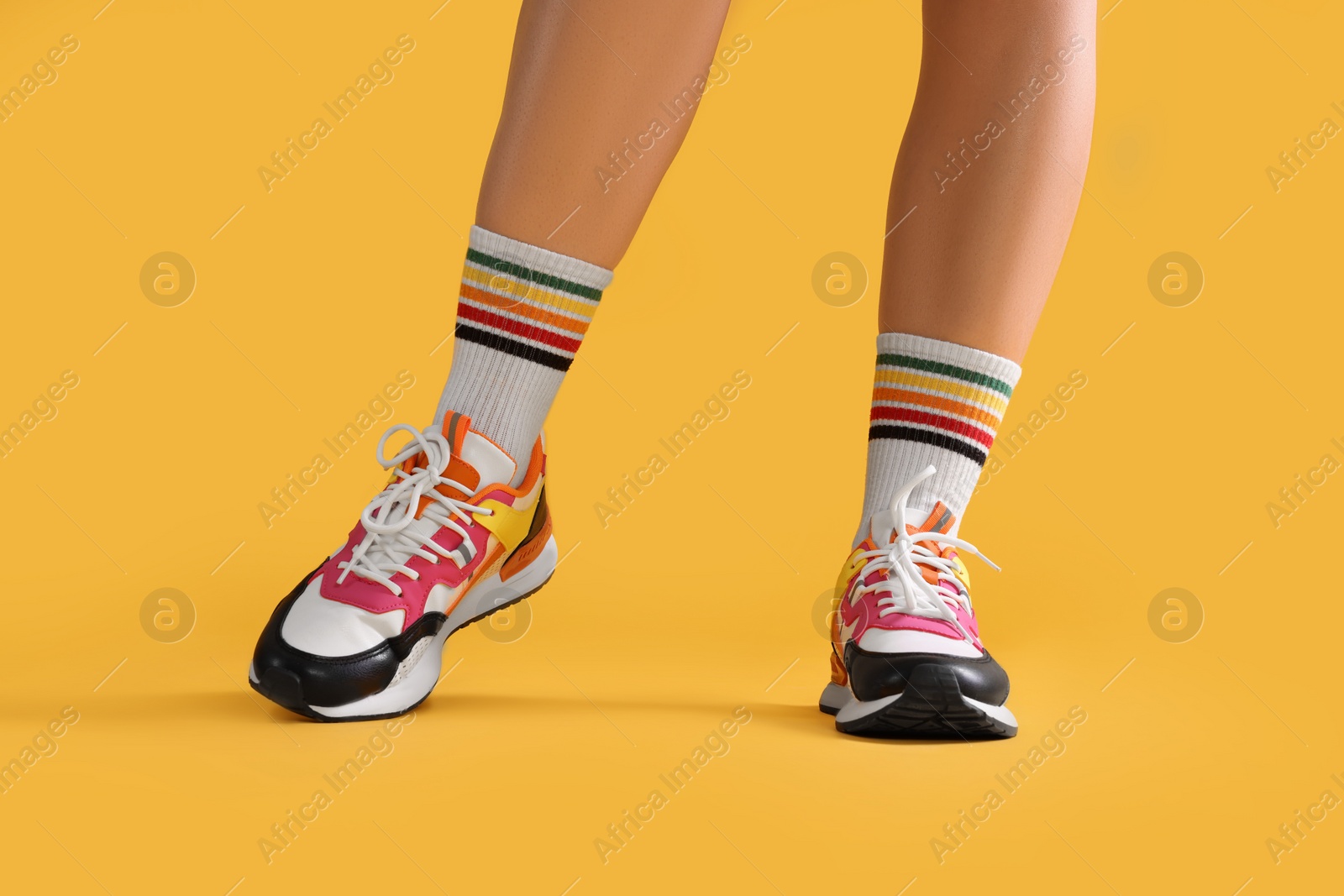 Photo of Woman wearing stylish sneakers on yellow background, closeup