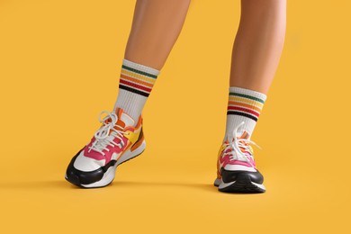 Photo of Woman wearing stylish sneakers on yellow background, closeup