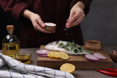 Woman salting raw dorado fish at grey table, closeup