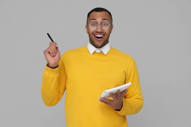 Emotional young intern holding notebook and pen on light grey background