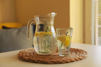 Photo of Jug and glass with refreshing lemon water on light table indoors