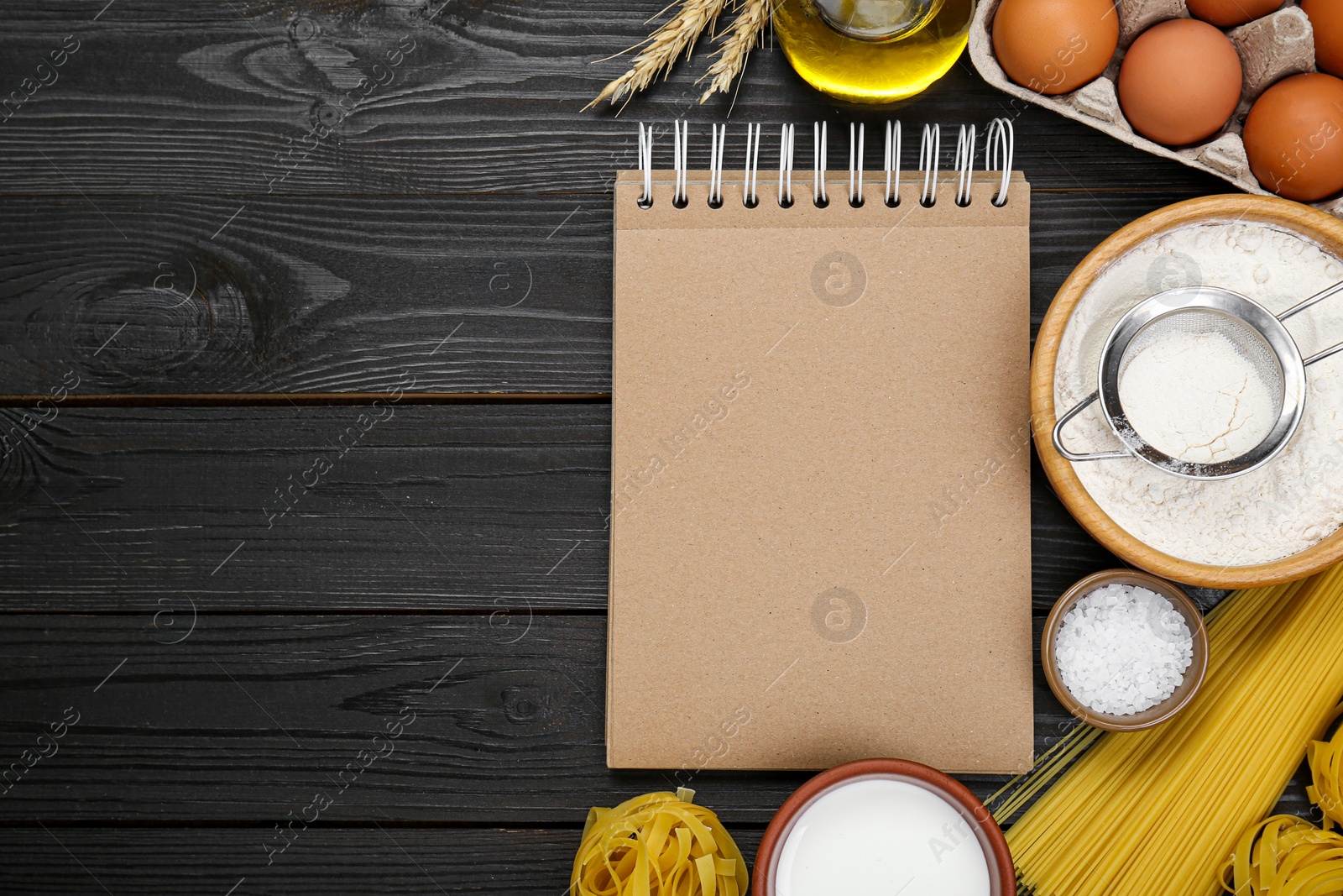 Photo of Blank recipe book and different ingredients on black wooden table, flat lay. Space for text