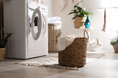 Photo of Wicker basket with laundry near washing machine indoors. Interior element