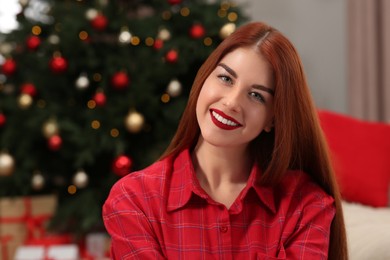 Beautiful young woman near Christmas tree indoors, space for text