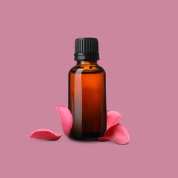 Image of Bottle of rose essential oil and flower petals on dusty pink background