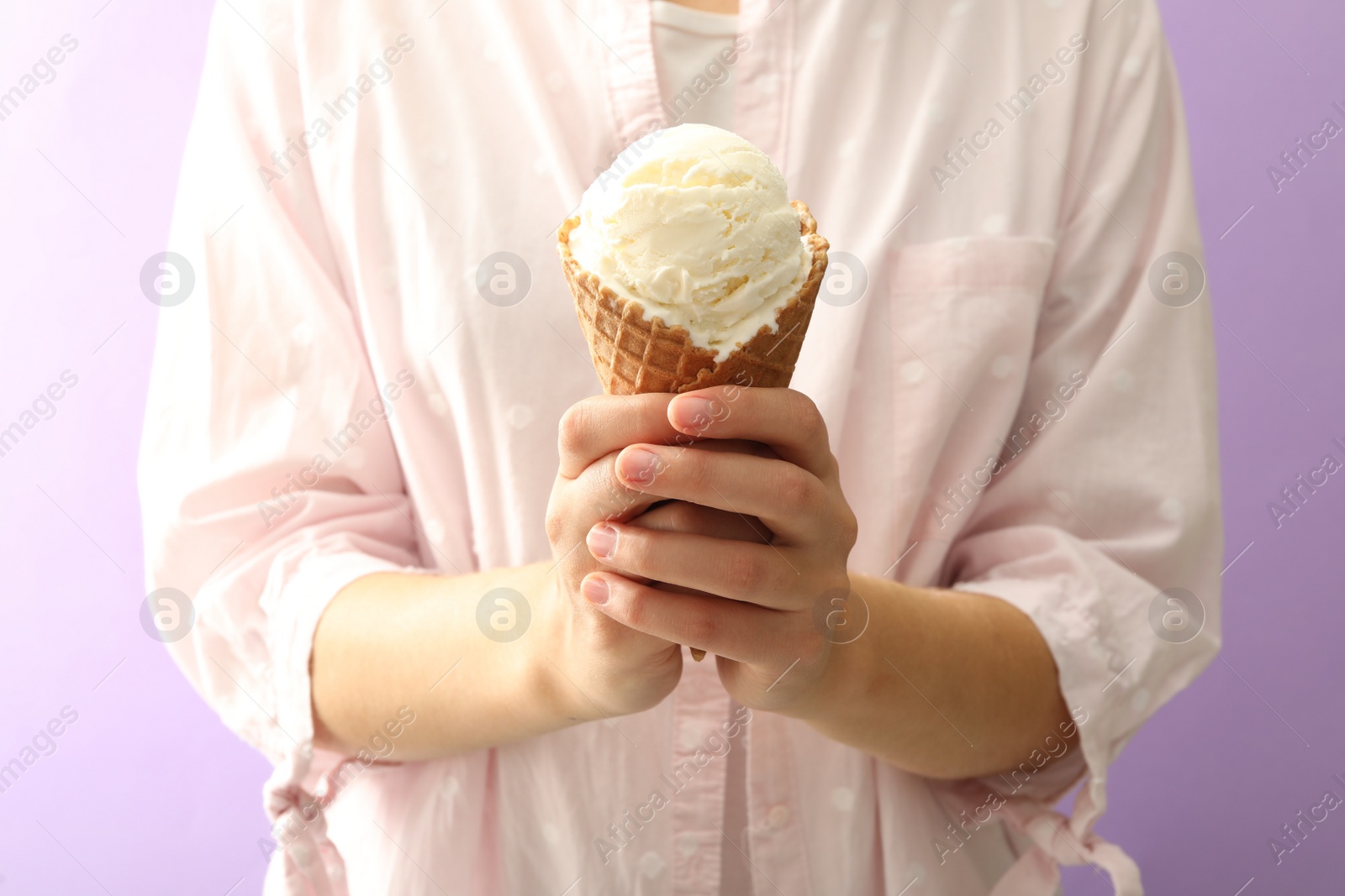 Photo of Woman holding white ice cream in wafer cone on violet background, closeup