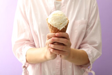 Photo of Woman holding white ice cream in wafer cone on violet background, closeup