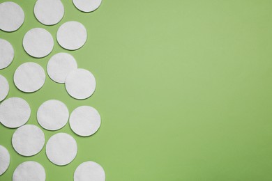 Many cotton pads on green background, flat lay. Space for text