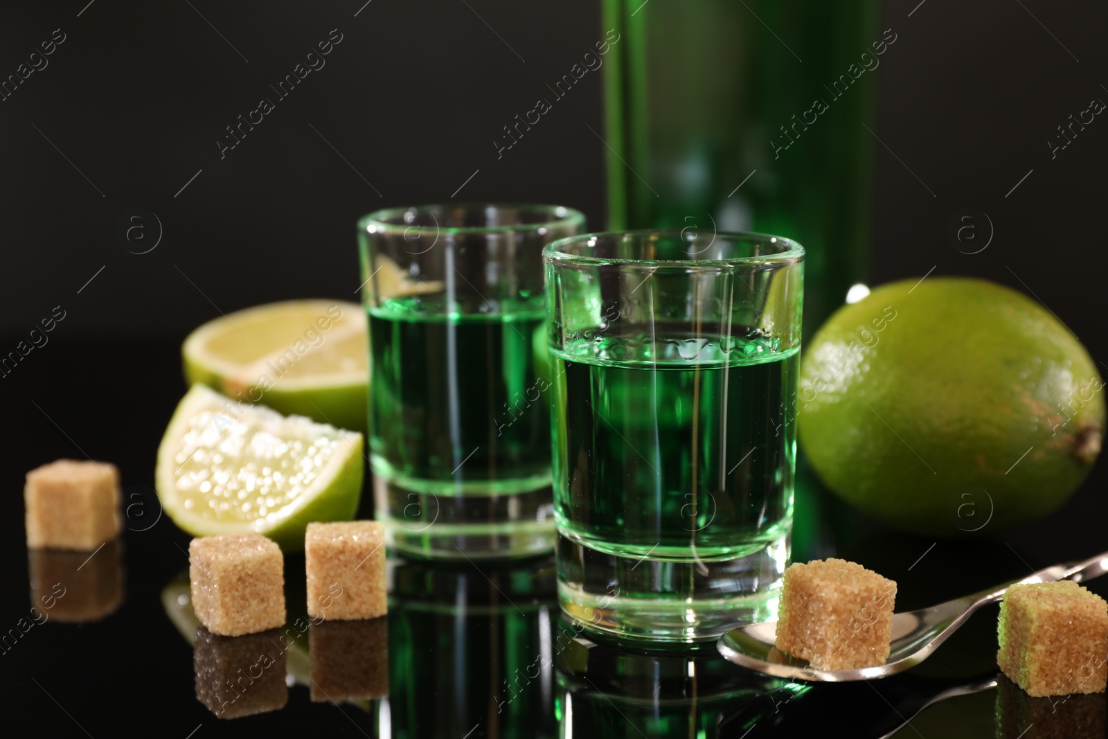 Photo of Absinthe in shot glasses, brown sugar, lime and spoon on mirror table. Alcoholic drink