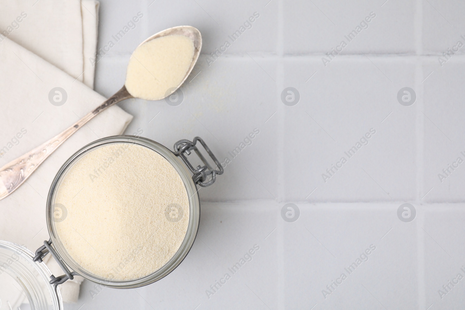 Photo of Uncooked organic semolina in jar and spoon on white tiled table, top view. Space for text