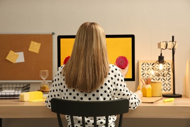 Photo of Woman sitting at wooden desk with computer near light wall, back view. Interior design