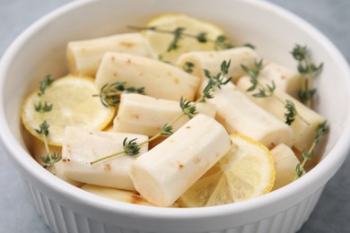Photo of Dish with raw salsify roots, lemon and thyme on table, closeup