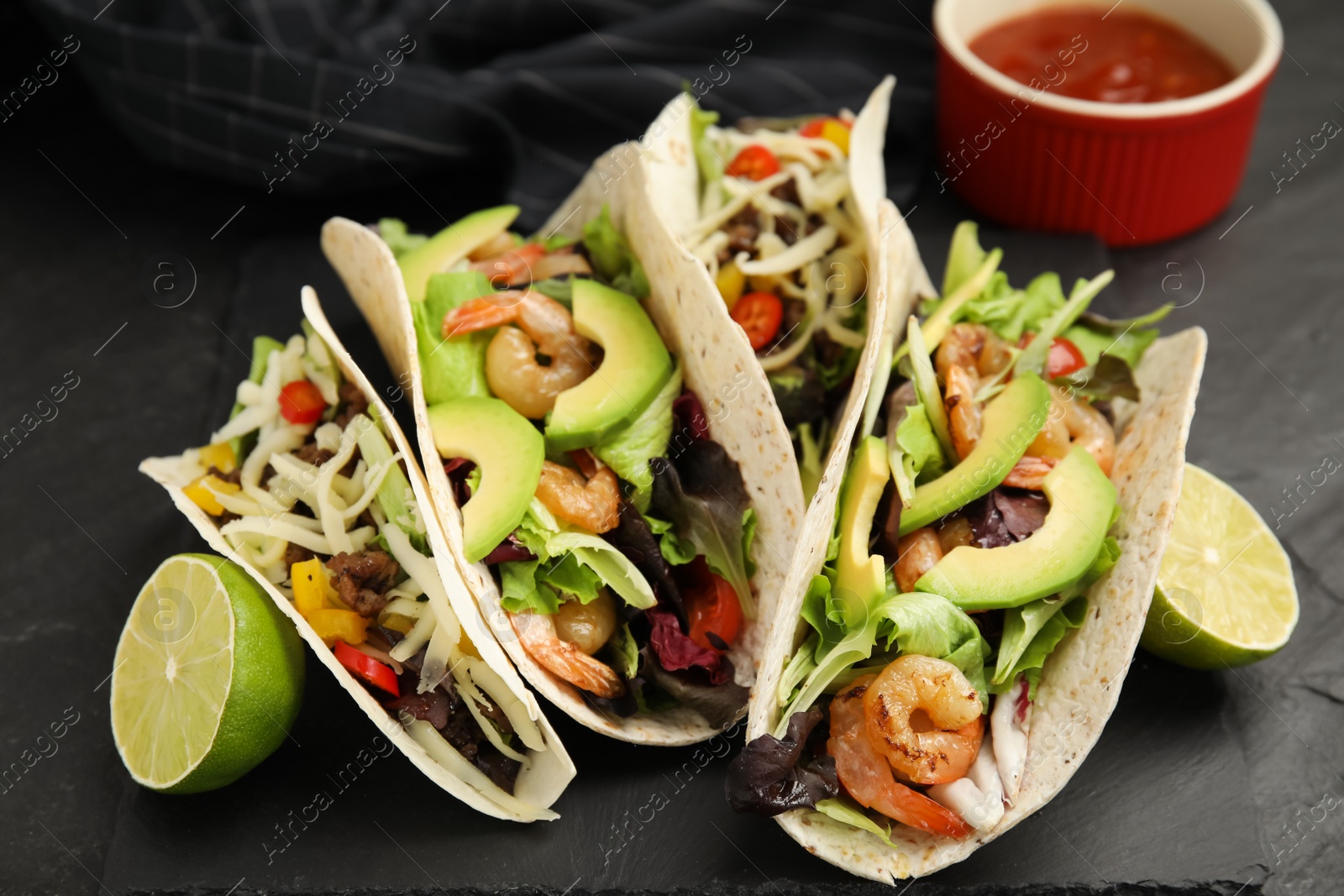 Photo of Delicious tacos, lime and sauce on black table, closeup