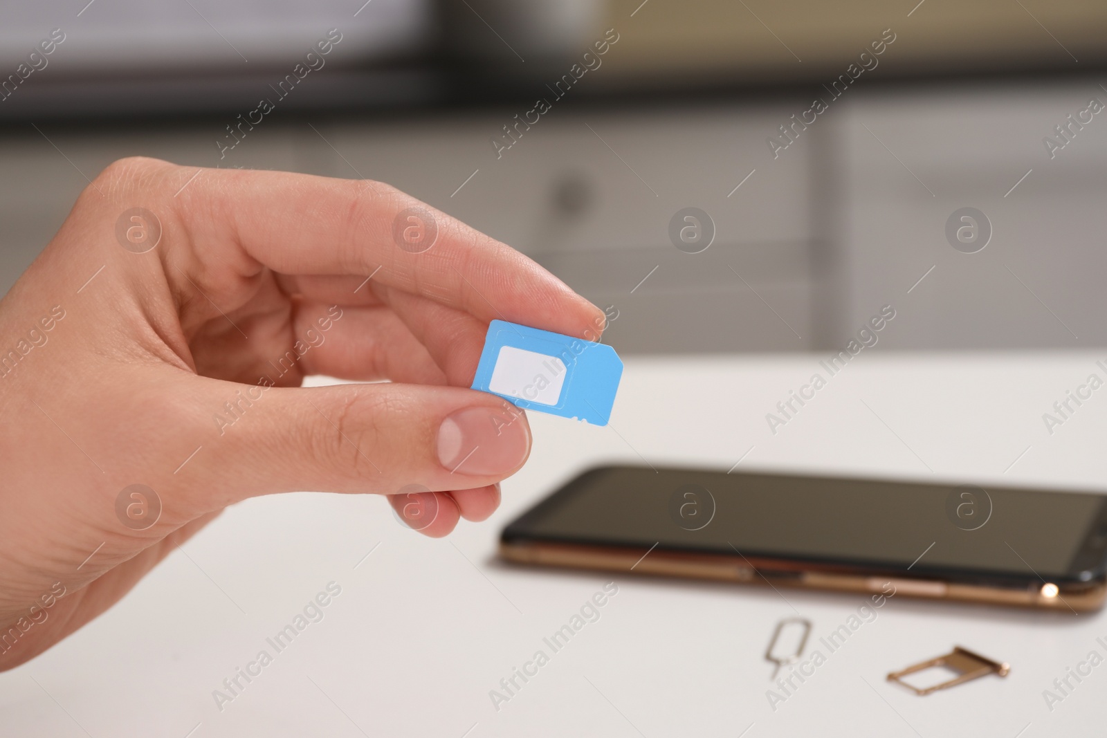 Photo of Woman with SIM card at white table indoors, closeup