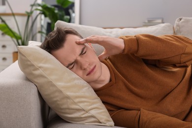 Sad man suffering from headache on sofa indoors