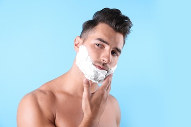 Photo of Handsome young man applying shaving foam on color background