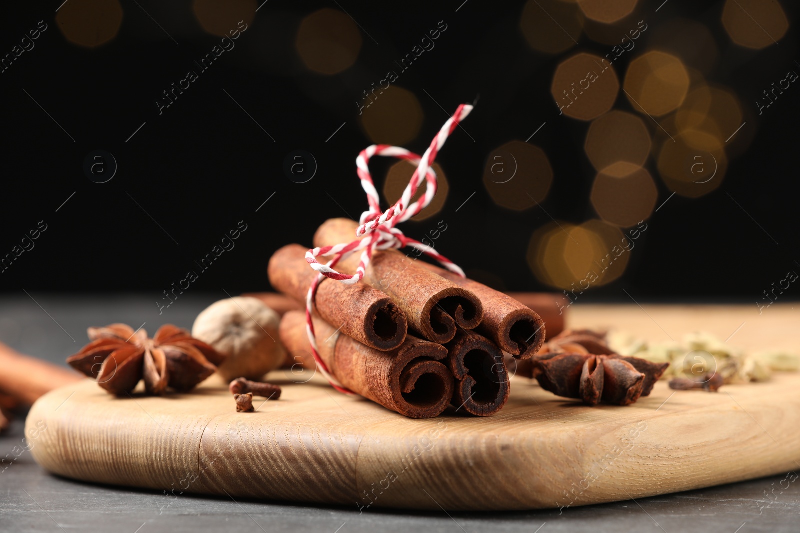 Photo of Cinnamon sticks and other spices on table against black background with blurred lights, closeup