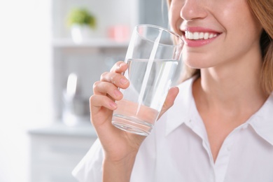Photo of Woman drinking clean water from glass in kitchen, closeup