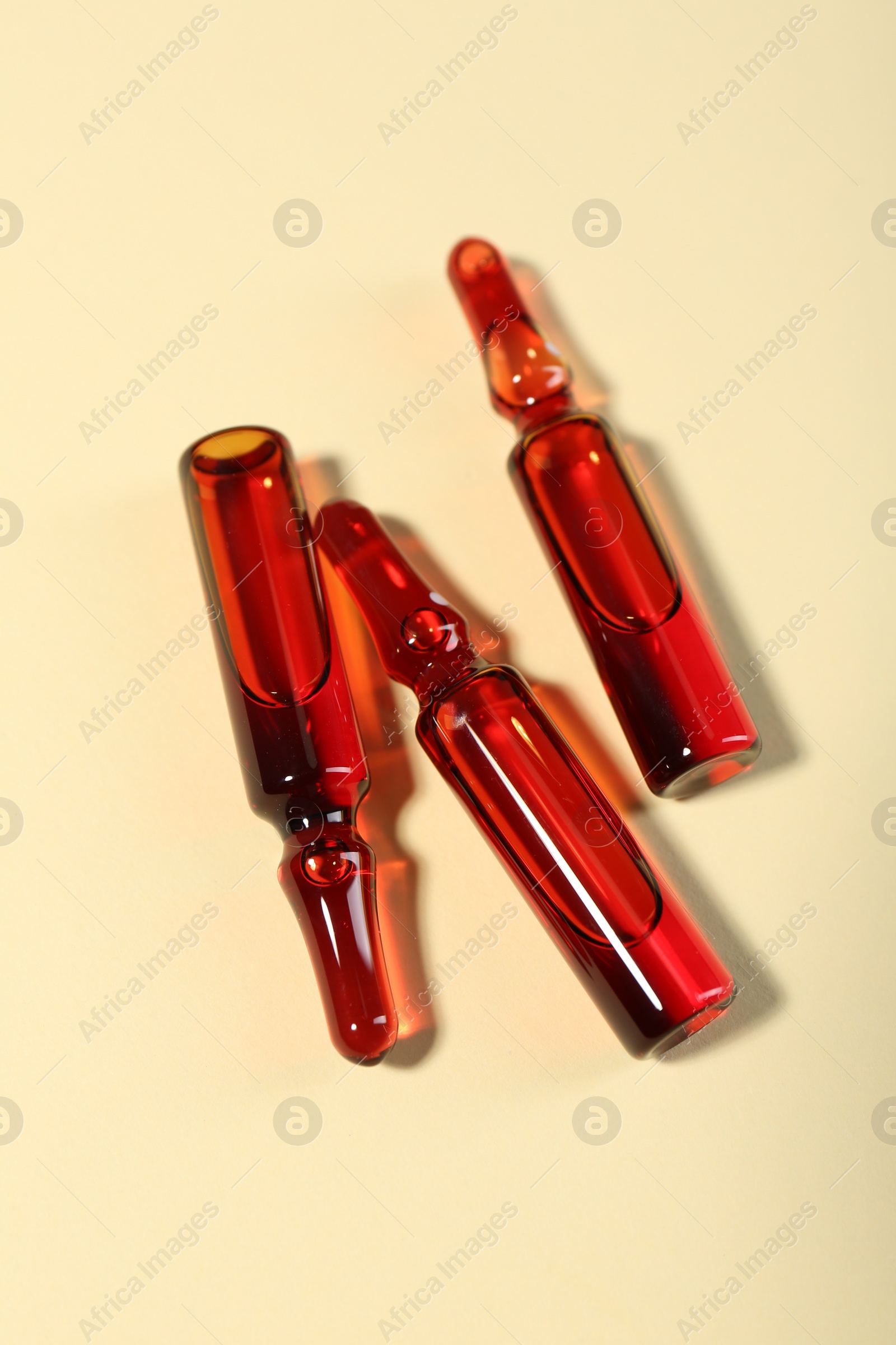 Photo of Glass ampoules with liquid on beige background, top view