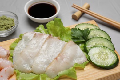 Photo of Sashimi set served with cucumber, lettuce, soy sauce and vasabi on light grey table, closeup