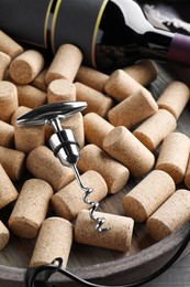 Photo of Corkscrew, wine bottle and stoppers on wooden tray, closeup