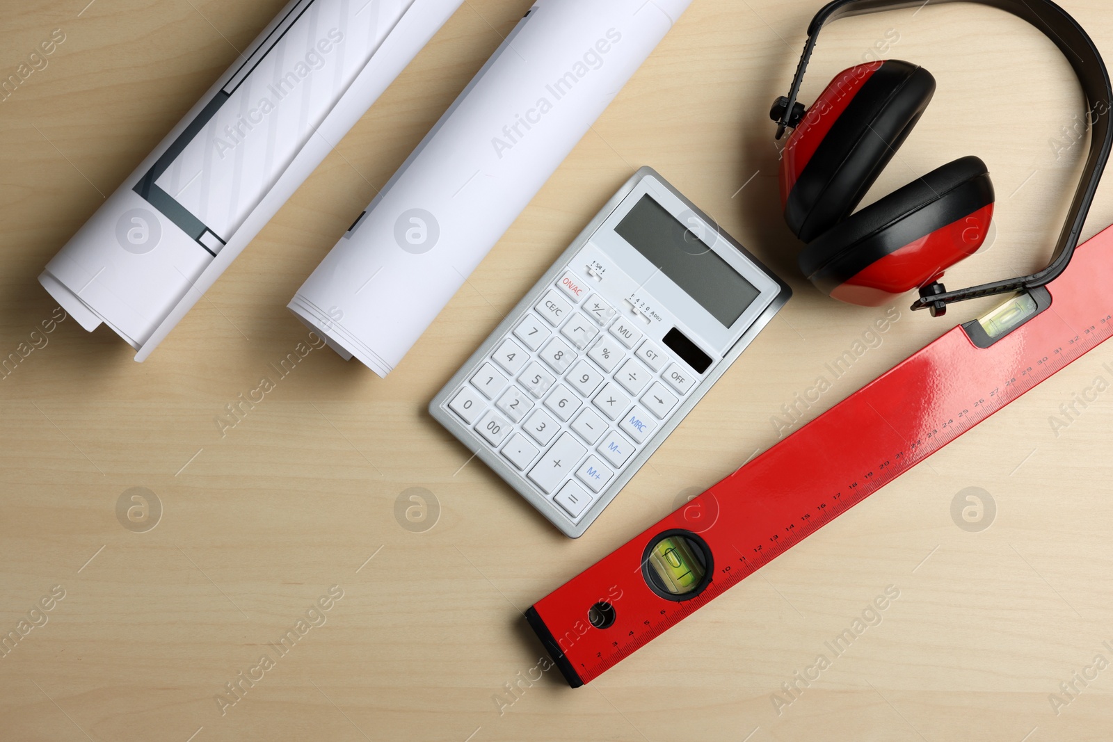 Photo of Construction drawings, safety headphones, calculator and bubble level on wooden table, flat lay