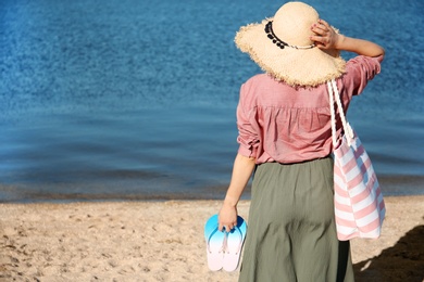 Photo of Woman with bag and flip-flops on beach. Space for text