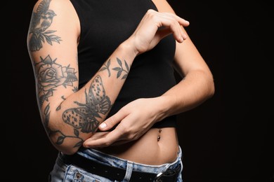 Woman with tattoos on arm against black background, closeup