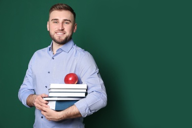 Portrait of young teacher with books and apple on green background. Space for text