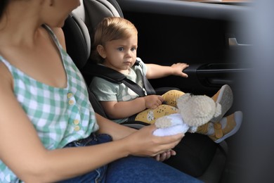 Photo of Woman with knitted toy near her daughter in child safety seat inside car