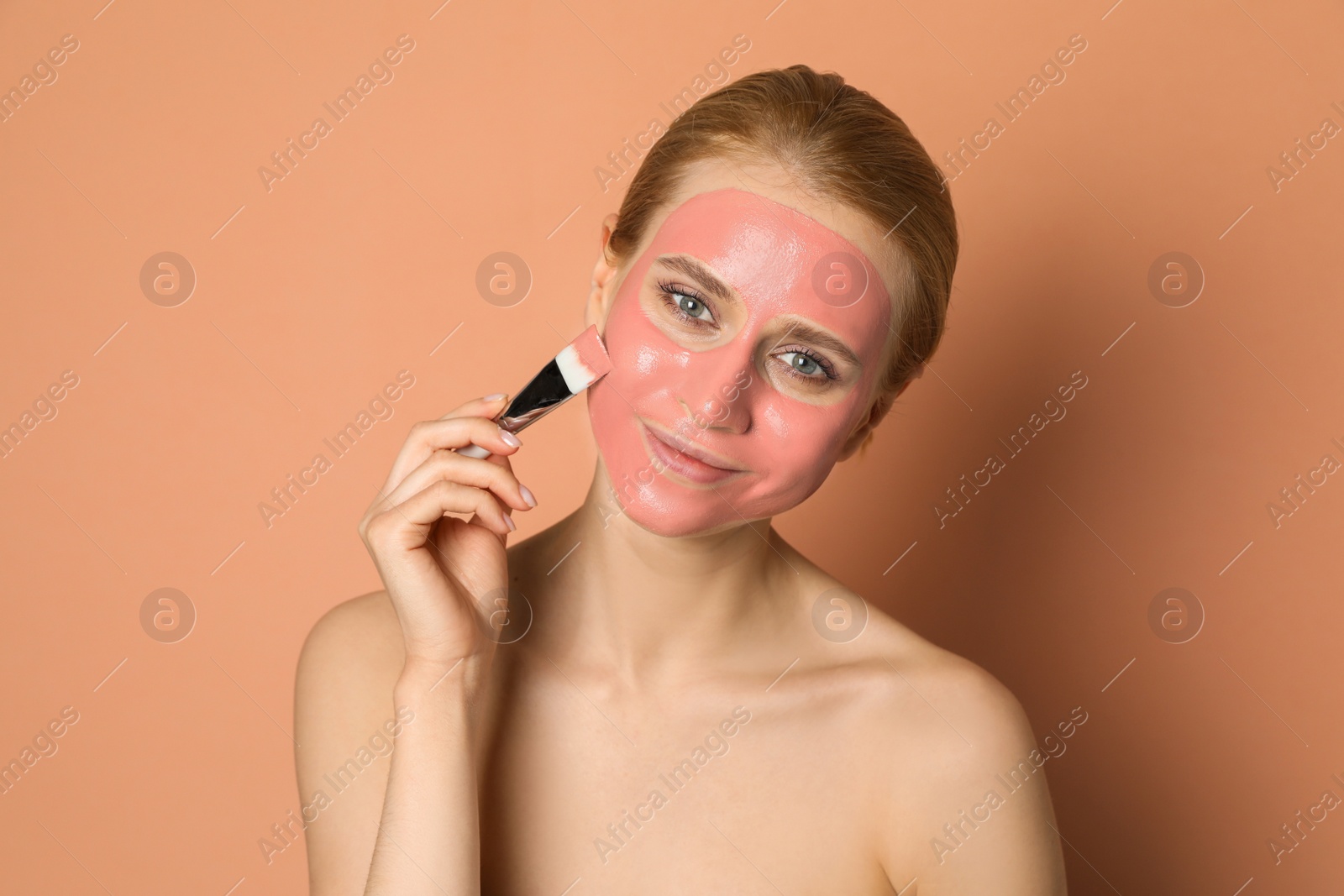 Photo of Young woman applying pomegranate face mask on pale coral background